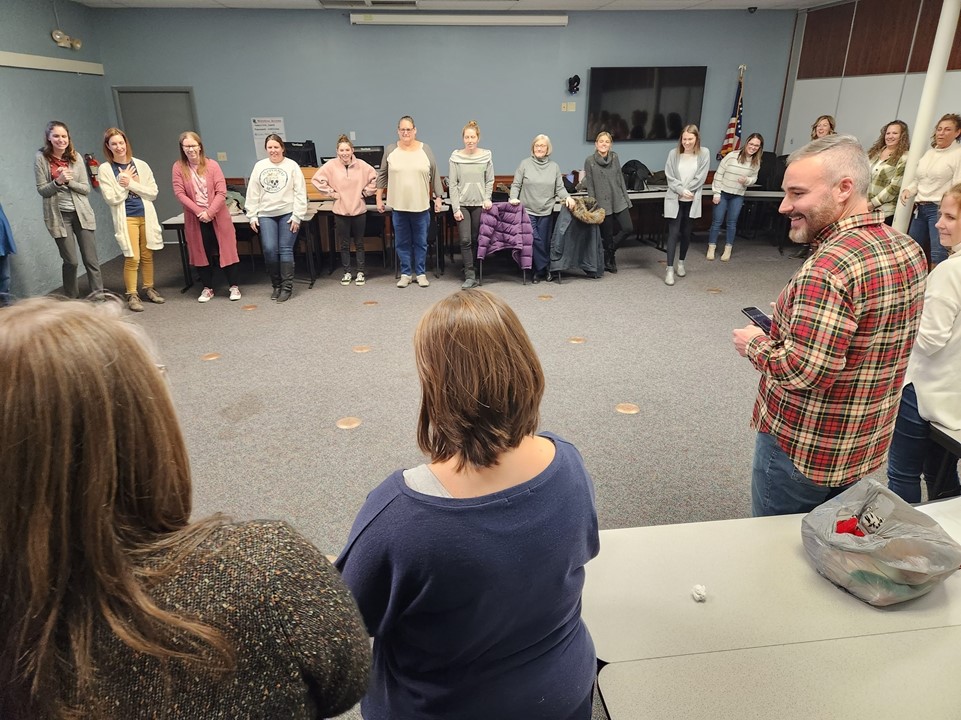 ladies standing in a big circle with a guy smiling as presenting